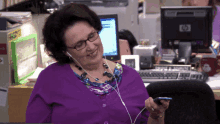 a woman wearing headphones looks at her phone in front of a hp monitor