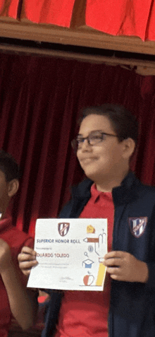 a young boy holds up a certificate that says superior honor roll