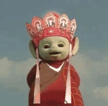 a green teletubbies doll wearing a red robe and a crown .