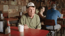 an older man sits at a table with a cup of coffee in front of a sign that says us 66