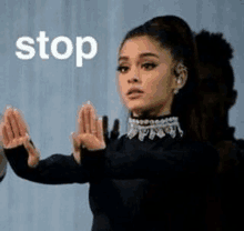 ariana grande is wearing a black dress and making a stop sign with her hands .