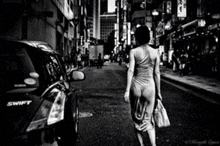 a black and white photo of a woman walking down a street next to a swift