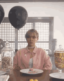 a woman in a pink jacket is sitting at a table with a plate of food in front of her