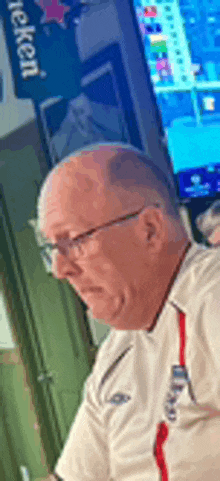 a bald man wearing glasses and a white shirt is sitting in front of a television .