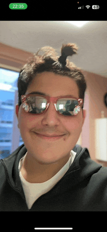 a young man wearing sunglasses and a ponytail smiles for a picture