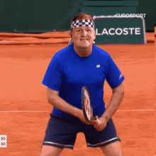 a man in a blue shirt is holding a tennis racket in front of a lacoste sign