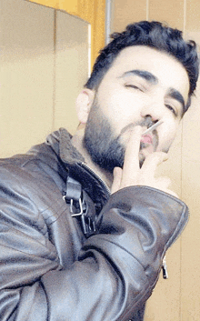 a man with a beard is smoking a cigarette and wearing a leather jacket