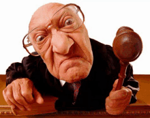 an elderly judge is holding a wooden gavel and looking at the camera .