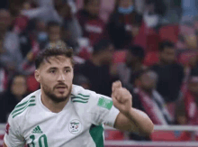 a man with a beard is wearing a white and green soccer jersey and giving a thumbs up .