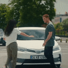 a man and a woman are standing in front of a white car with a license plate that says 34 kb 4190