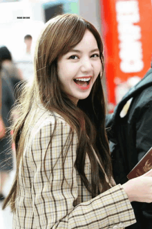 a woman wearing a plaid jacket is smiling and holding a passport in front of a sign that says food