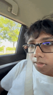 a young man wearing glasses and a seat belt is sitting in the back seat of a car .