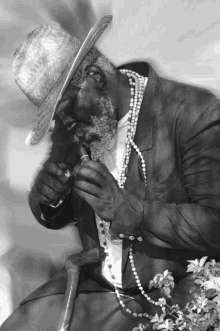 a black and white photo of a man wearing a straw hat and pearls