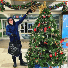 a man holding a black bag that says ' real planning ' on it stands in front of a decorated christmas tree