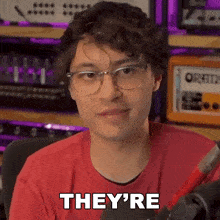 a young man wearing glasses and a red shirt is sitting in front of a microphone and says they 're .