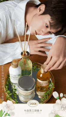 a man is laying on a wooden table with a tray of sabon products in front of him