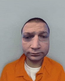 a man in an orange prison uniform is looking at the camera .