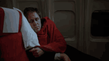 a man laying on an airplane with a red blanket