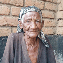 an elderly woman wearing a scarf around her head is smiling in front of a brick wall