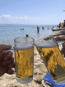 two glasses of beer with the letter m on them are being held on a beach