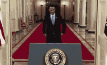 a man in a suit and tie is standing in front of a podium with the seal of the president of the united states .