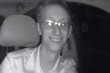 a black and white photo of a man wearing glasses sitting in a car .