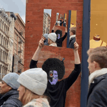 a man with a purple face is holding up a mirror in front of a brick building