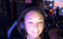 a girl wearing headphones looks at the camera with an american flag in the background