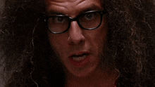 a man with curly hair wearing glasses looks at the camera