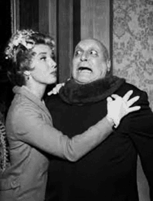 a black and white photo of a woman hugging a man with a scary face .