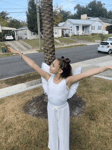 a girl dressed as an angel with her arms outstretched in front of a palm tree