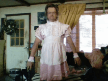 a man in a pink dress and apron is standing in a room