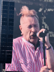 a man singing into a microphone wearing a pink and white striped shirt