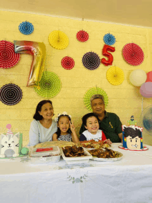 a family posing for a picture in front of a wall with balloons and decorations including a 7 and 5