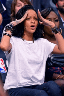 a woman in a white t-shirt is sitting in the stands at a basketball game with her hands on her head