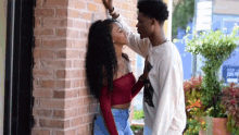 a man and a woman are kissing against a brick wall . the woman is wearing a red crop top .