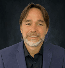 a man with a beard wearing a blue jacket and black shirt