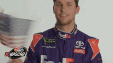 a man in a fedex racing suit is holding an american flag .