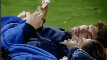 a man and a woman are laying on the grass and the man is holding a piece of paper