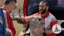 a man with a beard is holding a jerry can in front of a sign that says mi kis falunk