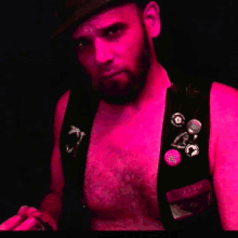 a man with a beard wearing a black vest with buttons on it and a pink background