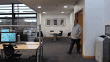 a man walking through an office with a trash can in front of him that says ' recycle ' on it