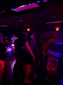 people are dancing in a dark room with a red exit sign