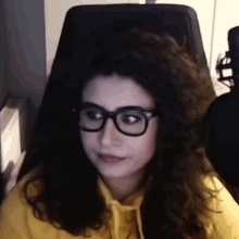 a woman wearing glasses and a yellow hoodie is sitting in front of a microphone .