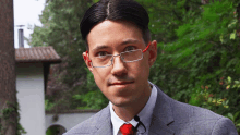 a man wearing glasses and a red tie stands in front of trees