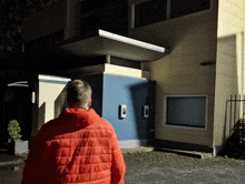 a man in an orange jacket stands in front of a large building