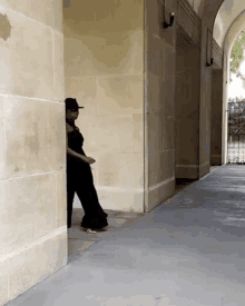 a woman in a black jumpsuit is standing behind a stone wall .