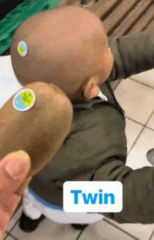 a baby with a sticker on his head and the word twin below him