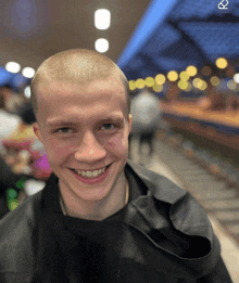 a young man with a shaved head is smiling in a blurry picture