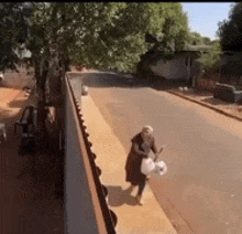 a woman is walking down a sidewalk holding a plastic bag